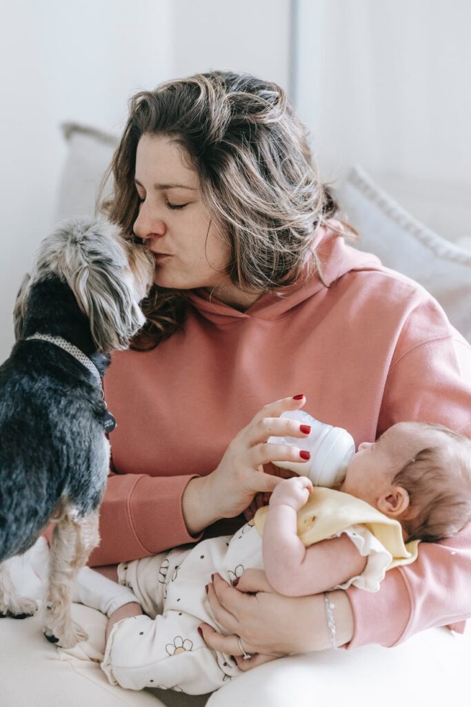 a woman is bottle feeding her baby and kisses her dog at the same time