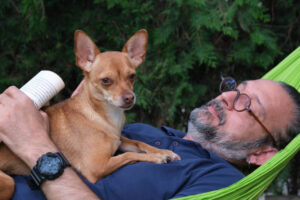 Man is with his dog in a green hammock on a summer day.